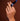 Hand wearing a pear-shaped diamond engagement ring holding a Royal Asscher navy ribbon on a warm brown background.