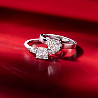 Two Royal Asscher diamond rings with step-cut square stones in white metal, displayed on a reflective red surface.