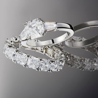 Royal Asscher eternity and engagement rings with Asscher Cut diamonds set in white gold, displayed on a gradient grey background.